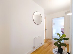 A hallway with a radiator, a round mirror, and a potted plant. - Two Bedroom Duplex Pent House in ExCeL (Greater London)