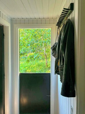 A room with a door leading to a green outdoor area, a coat rack with a jacket, and a black door.