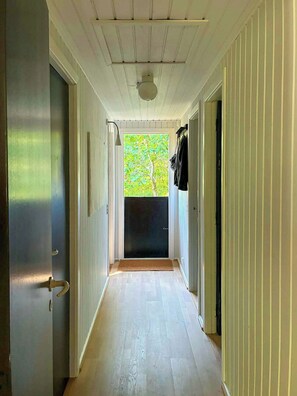 A narrow hallway with wooden floors, white walls, and a view of a tree through a door.