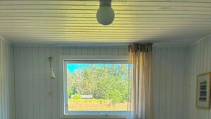 Una habitación con dos camas, una ventana que da a árboles, una mesita con una vela y una lámpara en el techo.