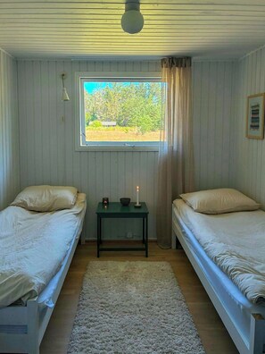 A room with two beds, a window with a view of trees, a small table with a candle, and a ceiling light.