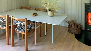 Un comedor con una mesa blanca, sillas estampadas con diseño de cebra, una lámpara colgante, una obra de arte abstracta enmarcada y un estufa de leña.