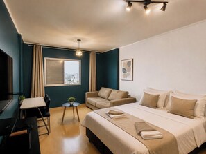 A hotel room with a bed, a desk, a chair, a small table with a plant, and a window with curtains. - Furnished apartment with garage and Wi-Fi in Santa Cecília – São Paulo (São Paulo)