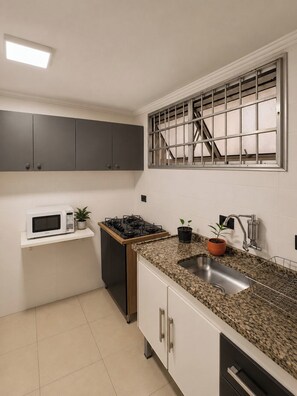 A compact kitchen with a microwave, stove, sink, and cabinets. - Furnished apartment with garage and Wi-Fi in Santa Cecília – São Paulo (São Paulo)