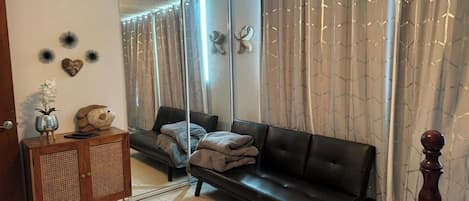 A living room with a black leather sofa, a wooden cabinet, and a mirror reflecting the room.
