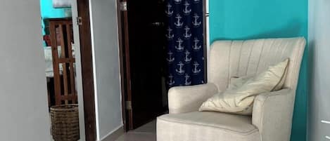 Ein beiges Sessel in einer Diele mit Fliesenboden, ein blauer Vorhang mit Anker-Muster und ein Holzregal mit Haken.