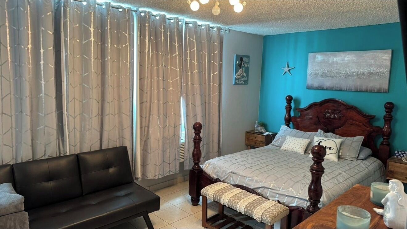 A bedroom with a bed, a wooden headboard, a bench, a bedside table, a nightstand, and curtains.