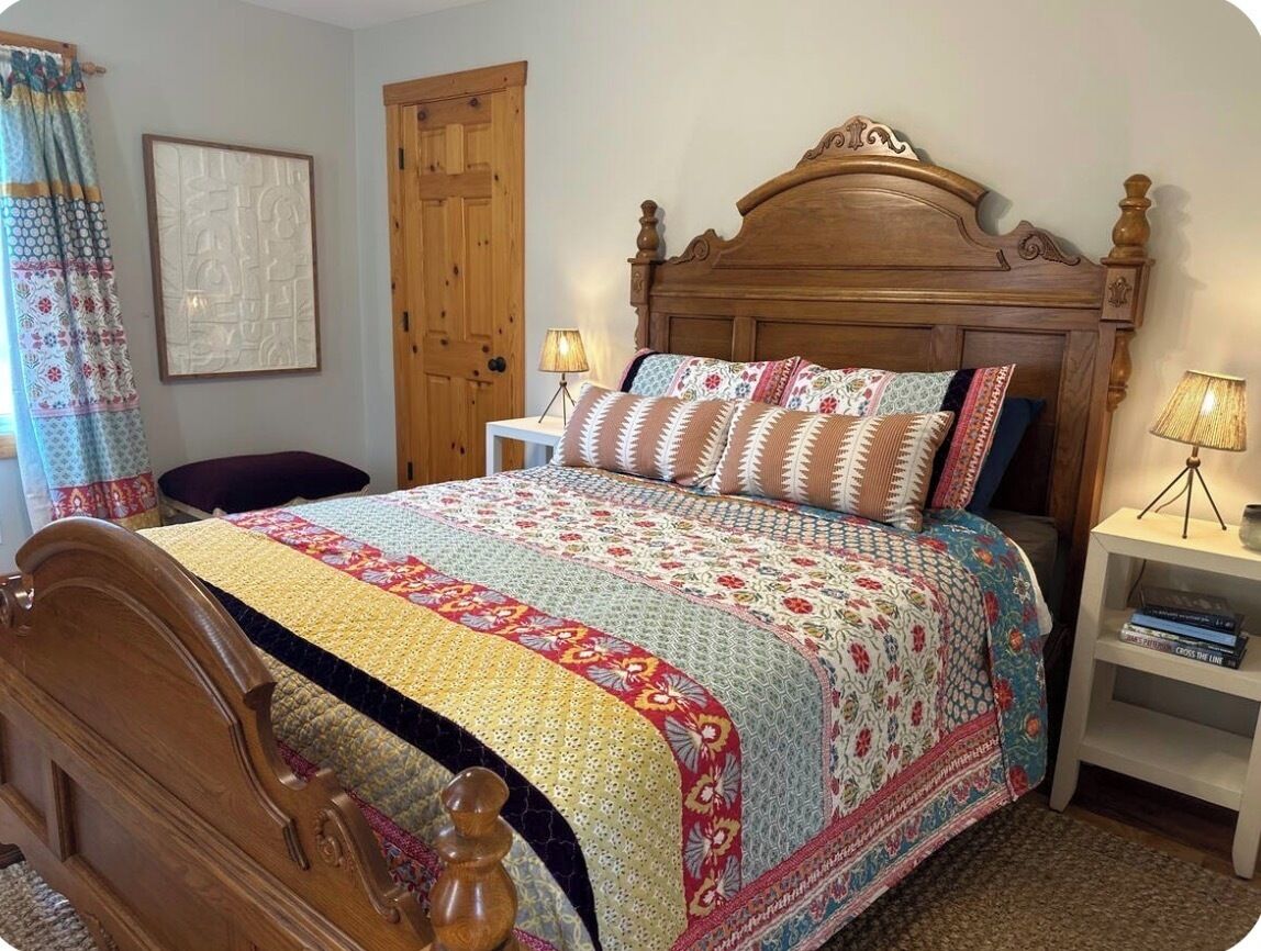 A bedroom with a wooden bed, a bedside table with a lamp, a door, and a curtain.