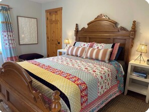 A bedroom with a wooden bed, a bedside table with a lamp, a door, and a curtain. - Redbird Waterfront Cottage with Dock and Hot Tub (Ashland City)