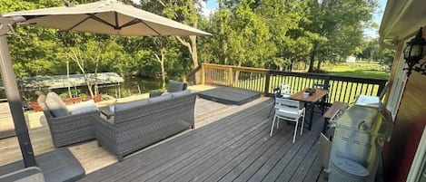 A wooden deck with outdoor furniture, a grill, and a view of a lake.