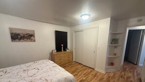 Quarto com cama, penteadeira, armário e prateleira com objetos decorativos.