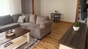 Uma sala de estar com sofá, mesa de centro e pequena mesa de jantar com cadeiras.