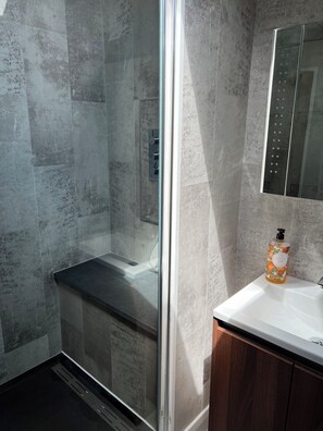 A modern bathroom with a glass-enclosed shower, a wooden vanity, and a marble-tiled wall. - Luxury Clifftop Beach House: Panoramic Sea Views, FREE Hot Tub & Games Room (Cayton Bay)
