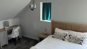 A bedroom with a bed, bedside table, lamp, desk, chair, and a window with curtains. - Luxury Clifftop Beach House: Panoramic Sea Views, FREE Hot Tub & Games Room (Cayton Bay)