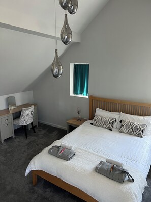 A bedroom with a bed, bedside table, lamp, desk, chair, and a window with curtains. - Luxury Clifftop Beach House: Panoramic Sea Views, FREE Hot Tub & Games Room (Cayton Bay)