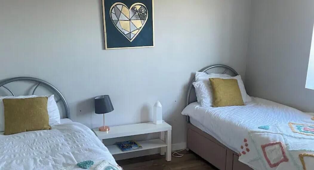 Quarto com duas camas, uma mesa de cabeceira, uma luminária e uma obra de arte na parede.