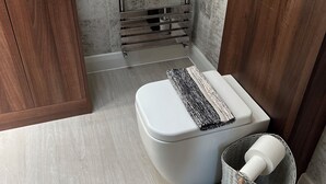 A modern bathroom with a white toilet, a wooden cabinet, a chrome towel rack, and a wicker waste basket. - Luxury Clifftop Beach House: Panoramic Sea Views, FREE Hot Tub & Games Room (Cayton Bay)