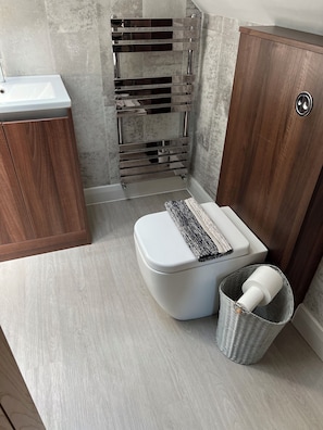 A modern bathroom with a white toilet, a wooden cabinet, a chrome towel rack, and a wicker waste basket. - Luxury Clifftop Beach House: Panoramic Sea Views, FREE Hot Tub & Games Room (Cayton Bay)