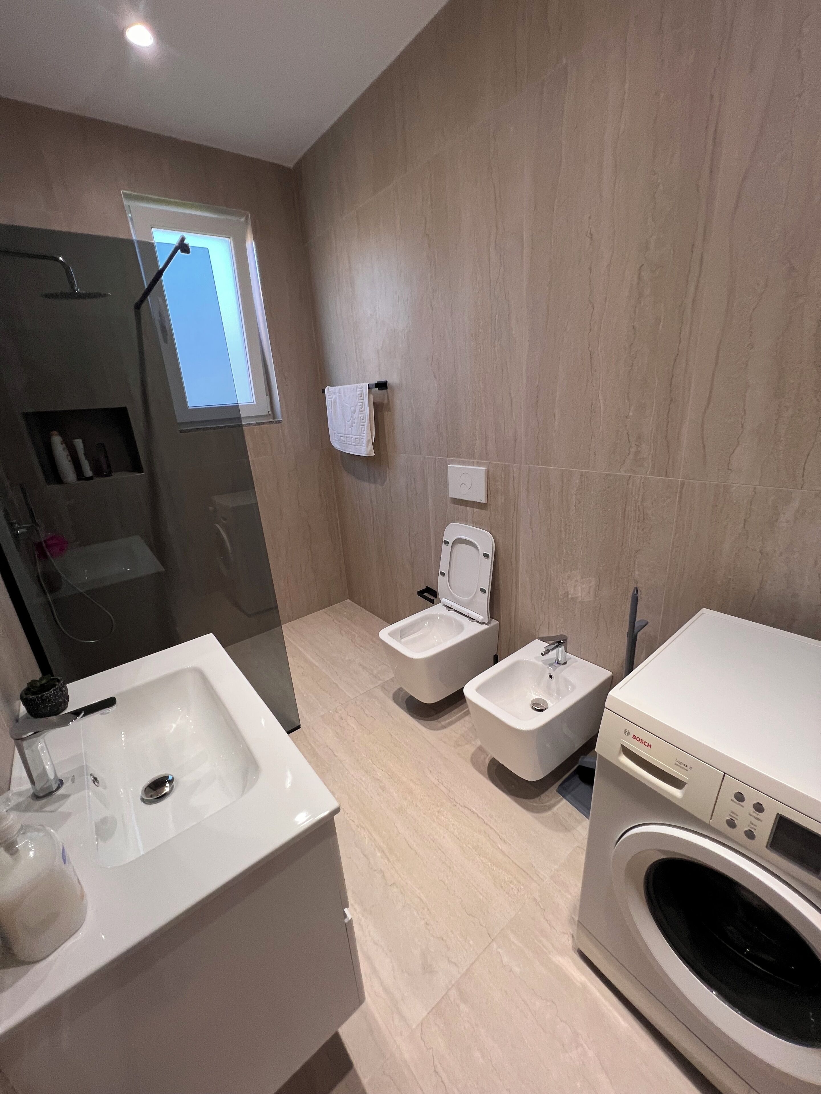 Een moderne badkamer met een wastafel, toilet en wasmachine.