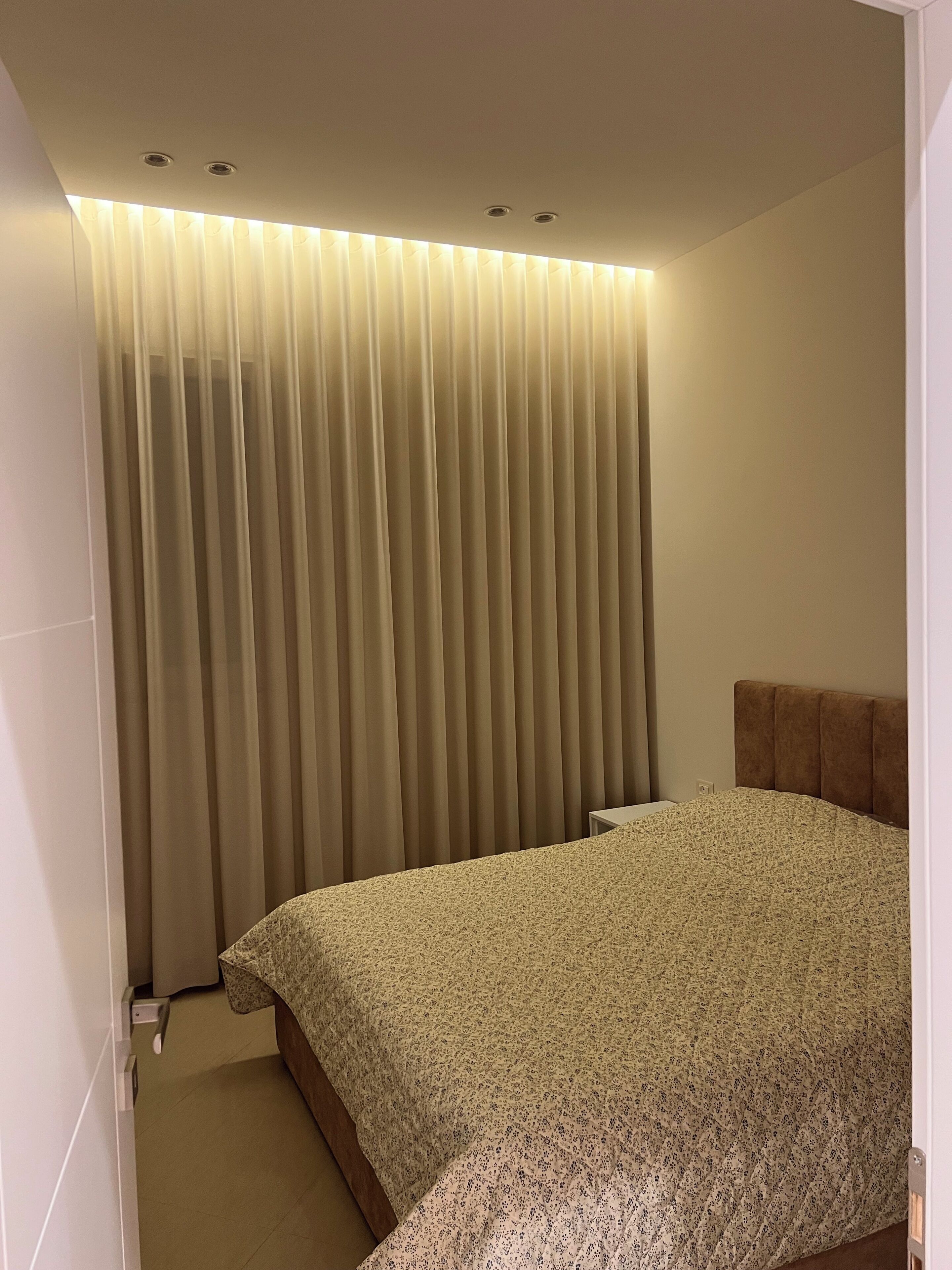 A bedroom with a bed, a headboard, a curtain, and a ceiling light fixture.