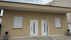 Ein Gebäude mit zwei weißen Türen, einer beige farbenen Fassade und einem Betonfundament.