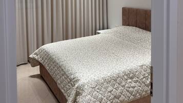 Una camera da letto con un letto, una testiera, una finestra con tende e faretti a soffitto.