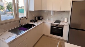 Eine moderne Küche mit weißen Schränken, einem Edelstahlkühlschrank, einem eingebauten Backofen und einem Fenster mit Jalousien.