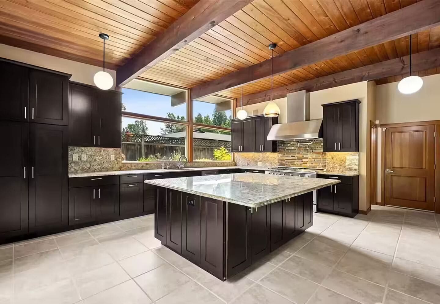 A modern kitchen with dark cabinetry, a large island, and a stone backsplash.