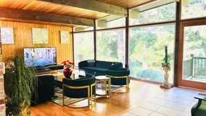 A modern living room with a television, black sofas, and a large window with a view of greenery. - Northwest Elegance – Modern Retreat (Normandy Park)