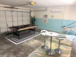 A pool table with a green felt surface, two white bar stools, and a ceiling-mounted projector. - Modern Home w Pool / Jaccuzi / Game Room - 8PPL (Seminole)