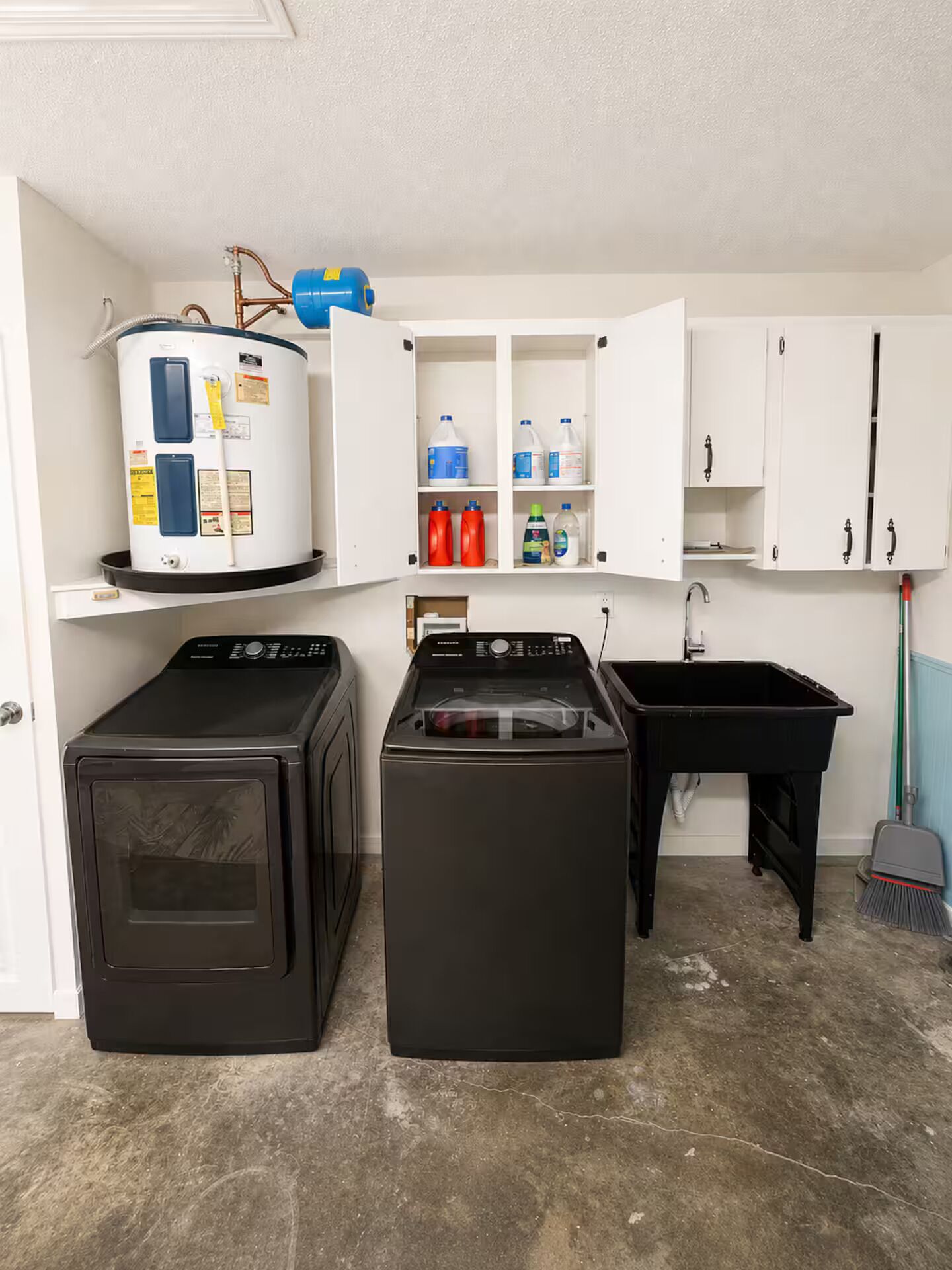 A laundry room with two washing machines, a water heater, and a sink.