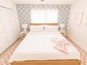 Hotellihuone, jossa on sänky, kaksi yöpöytää, yölamppu, vaatekaappi ja ikkuna, jossa on verhot.