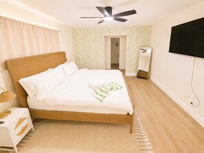 Ein Schlafzimmer mit einem Bett, einem Deckenventilator, einem Fernseher und einer Tür zu einem anderen Raum.