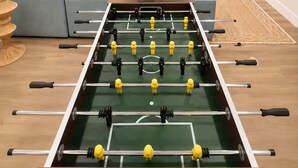 Un soggiorno con un tavolo da calcio, un divano, una televisione e una TV a parete.