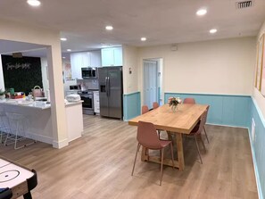 Eine moderne Küche mit weißen Schränken, einem Edelstahl-Kühlschrank und einem Essbereich mit Holztisch und rosa Stühlen.