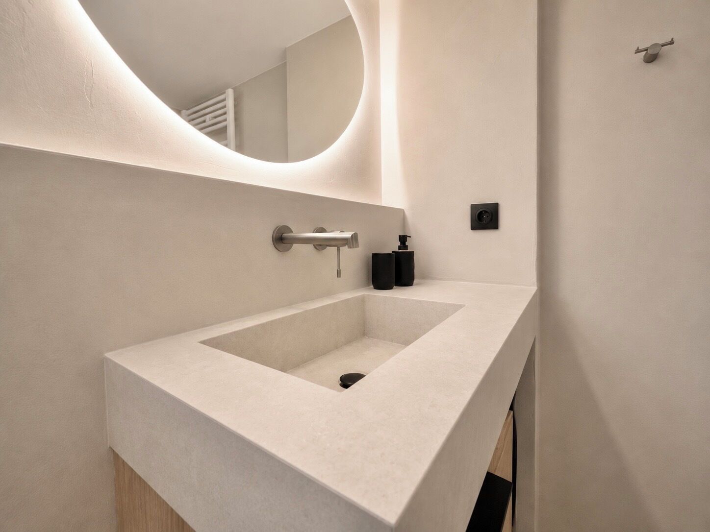 A modern bathroom with a large rectangular sink, a wall-mounted mirror, and a small black soap dispenser.