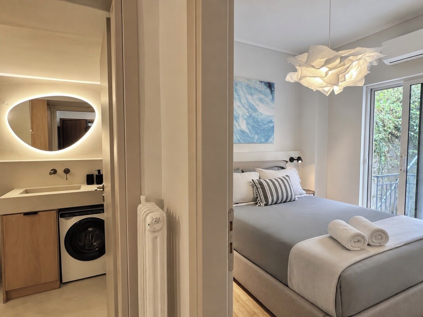 Une chambre moderne avec un grand lit, un lave-linge, une salle de bain avec un miroir et une vue sur la verdure.