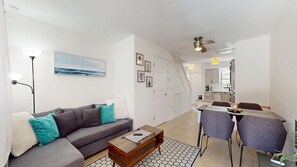 Ein modernes Wohnzimmer mit einer grauen Couch, einem Holztisch und einem Essbereich mit zwei Stühlen und einem Tisch.