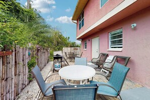 Eine Terrasse mit einem runden Tisch und Stühlen, einem Holzzaun und einem Gebäude mit rosa Fassade.