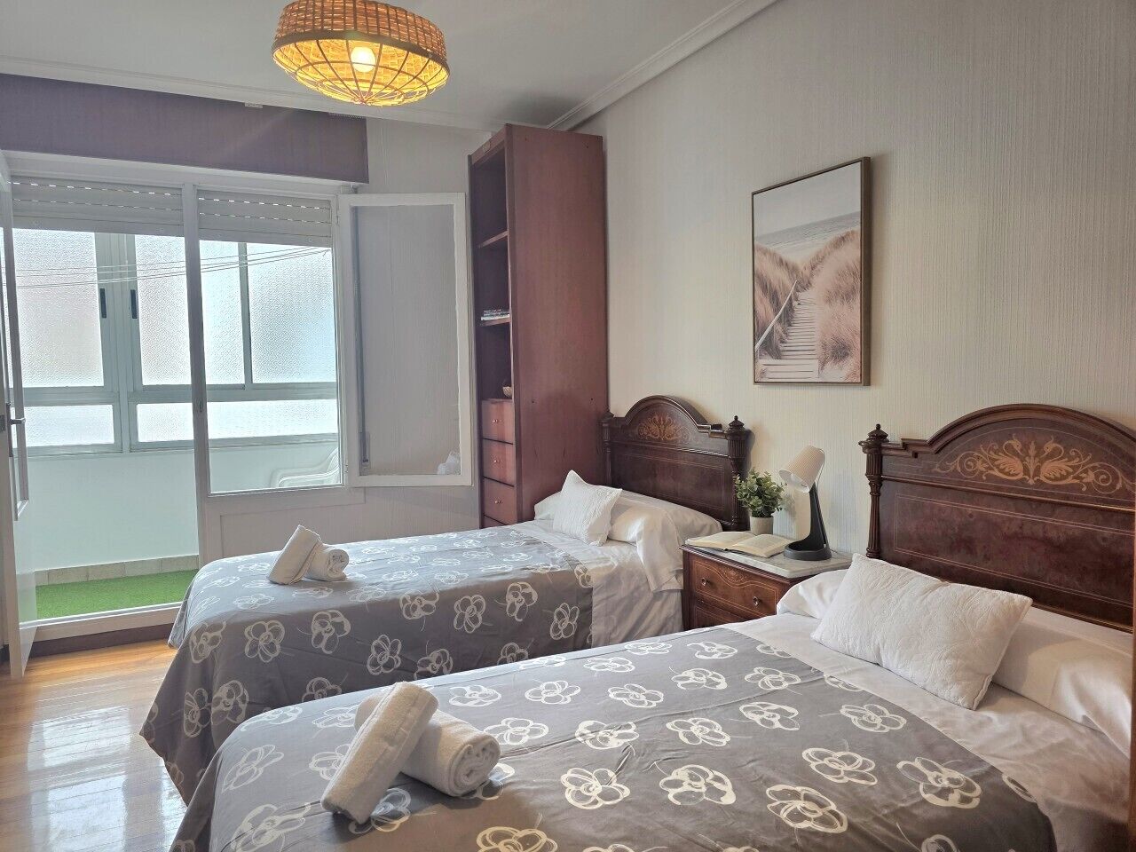 A hotel room with two beds, a wooden headboard, a window with a view, and a door leading outside.