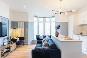 Una sala de estar moderna con un televisor grande, un sofá y un comedor con mostrador de cocina.
