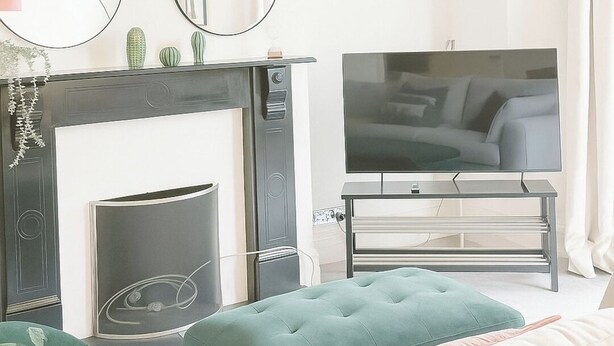 Un salon moderne avec une cheminée, un téléviseur à écran plat, un pouf vert et un grand miroir.