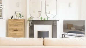 Un salon avec une cheminée, un canapé, un meuble en bois et deux miroirs fixés au mur.