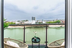 A balcony with wicker chairs, a small table with a plant, and a view of a cityscape across a body of water. - The Riverside Haven – City Centre + Parking (Newport)
