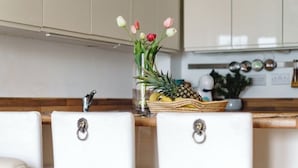 A kitchen with two white bar stools, a wooden countertop, and a vase with flowers. - The Riverside Haven – City Centre + Parking (Newport)