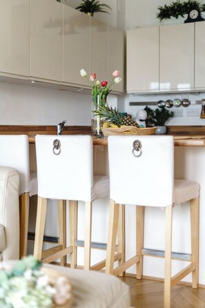Eine Küche mit zwei weißen Barhocker, einer Holz Arbeitsplatte und einer Vase mit Blumen.