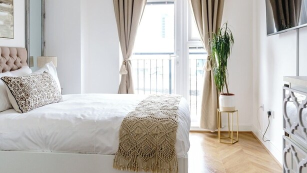 A bedroom with a bed, a chandelier, curtains, a plant, and a TV. - The Riverside Haven – City Centre + Parking (Newport)