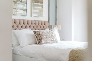 A neatly made bed with a tufted headboard, white bedding, and patterned pillows. - The Riverside Haven – City Centre + Parking (Newport)