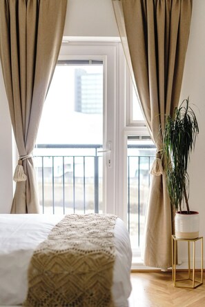 Ein Schlafzimmer mit Bett, Vorhängen, einer Topfpflanze und Blick durch eine offene Tür.