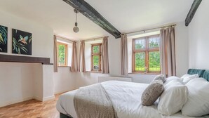 Ein Schlafzimmer mit einem großen Bett, Holzboden, zwei Fenstern mit Vorhängen und einer Hängelampe.